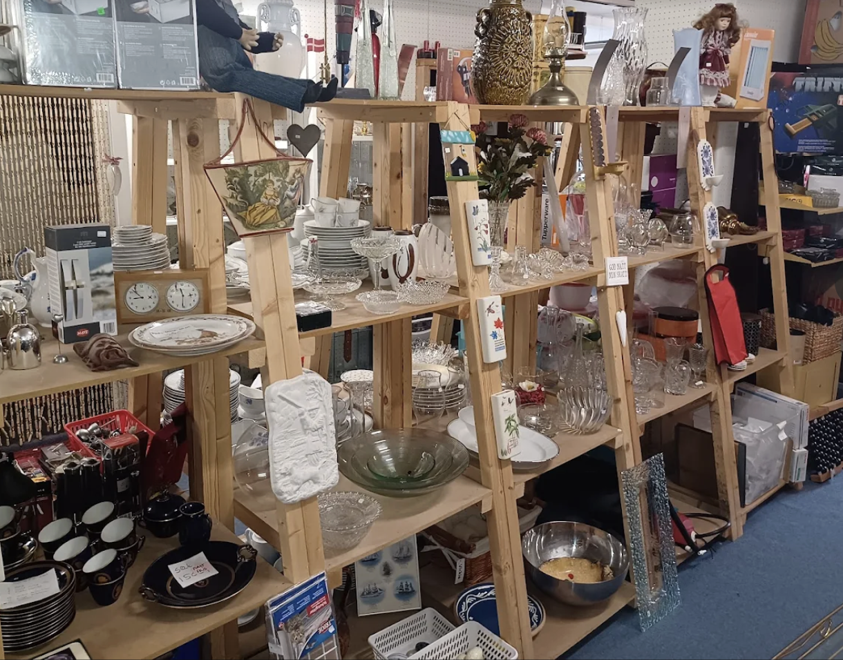 Antikviteter, glas og loppefund udstillet på hylder inde i genbrugsbutikken i Sommersted